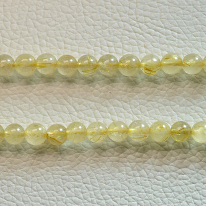 Gold Rutilquarz Perlenkette aus 6mm Naturstein – Kristallschmuck mit Metallverschluss und goldenen Rutilnadeln. Nah.