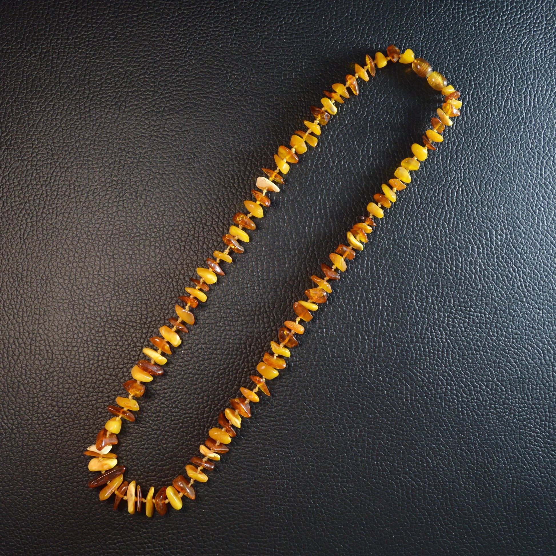 Mehrfarbige Bernstein Kette 55 cm – Gesamtansicht liegend, natürlicher Glanz der Steine und Drehverschluss erkennbar.